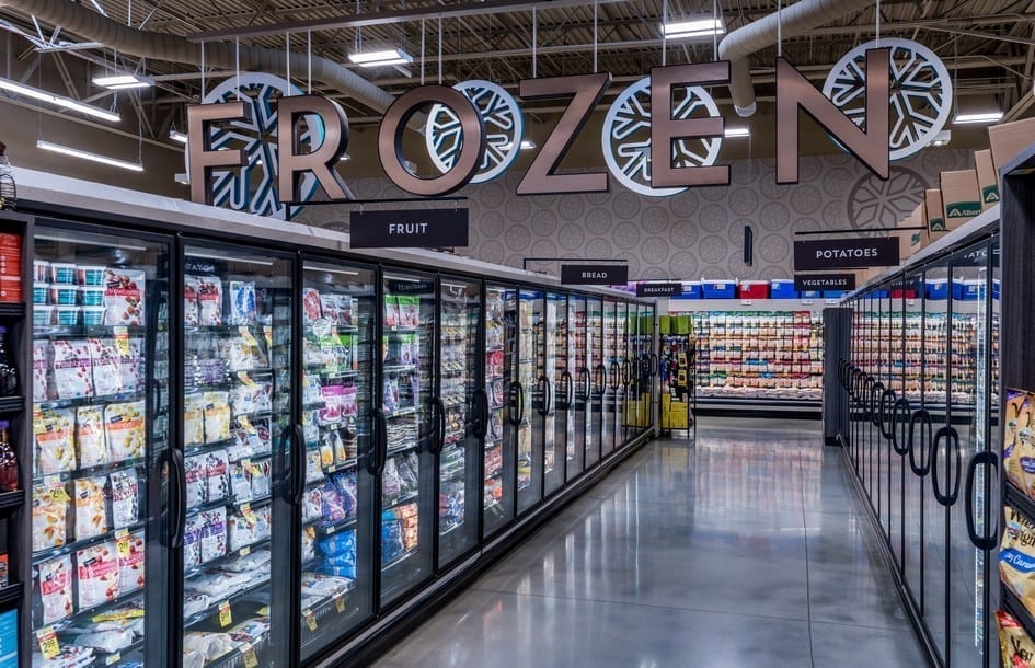 Freezer aisle of a grocery store with large hanging letters spelling out "FROZEN". Behind the letters are a set of ice crystal, a pattern repeated on the wall at the end of the aisle.