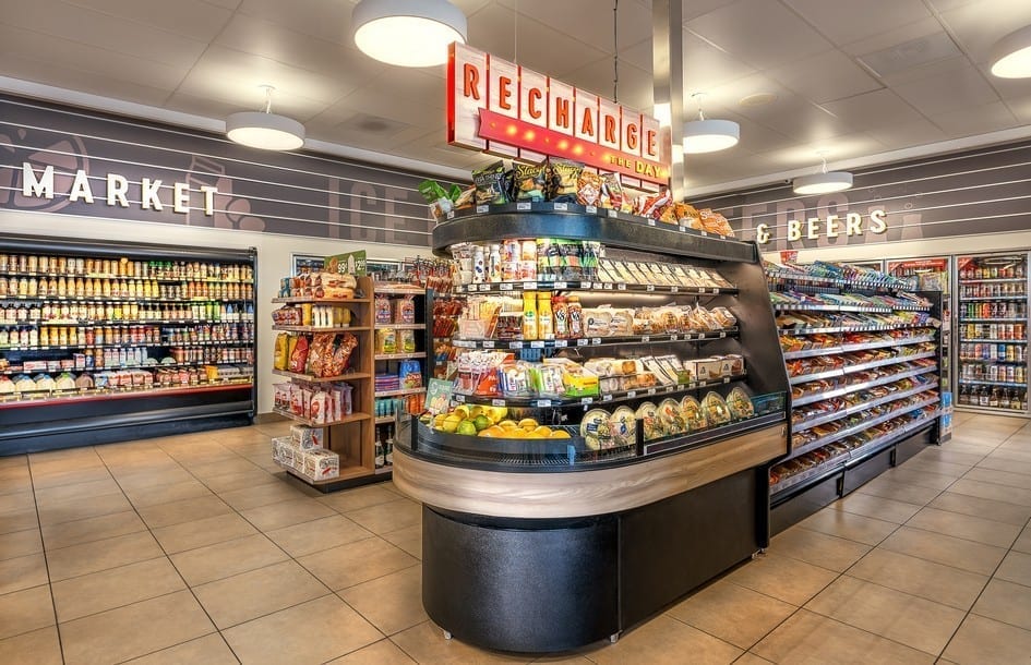 The carefully planned interior layout of a convenience store showcases wide allows, a grab and go case, clear signage, and a vast assortment of products.