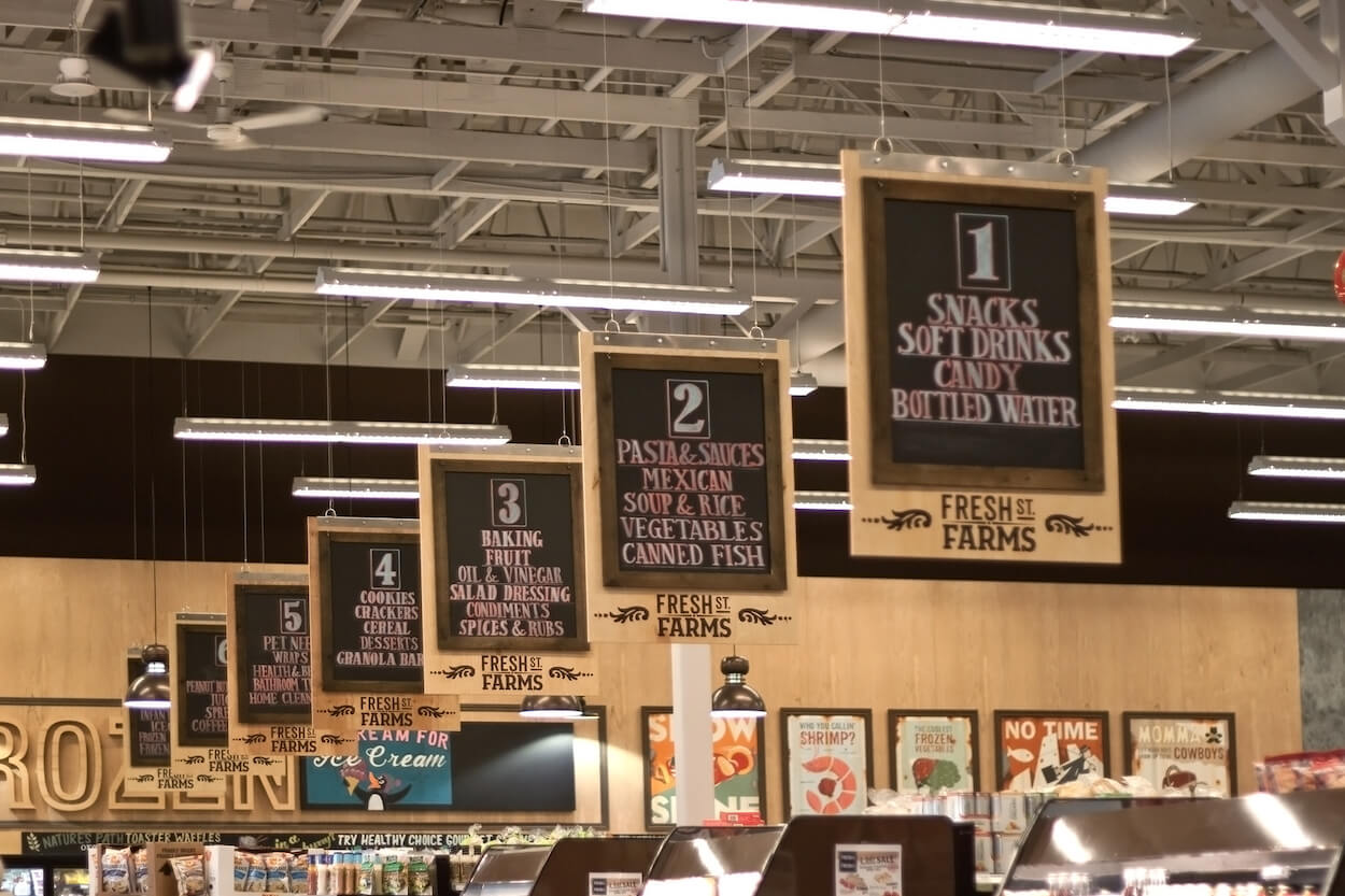 A grocery store with a aisle markers hanging from the ceiling.
